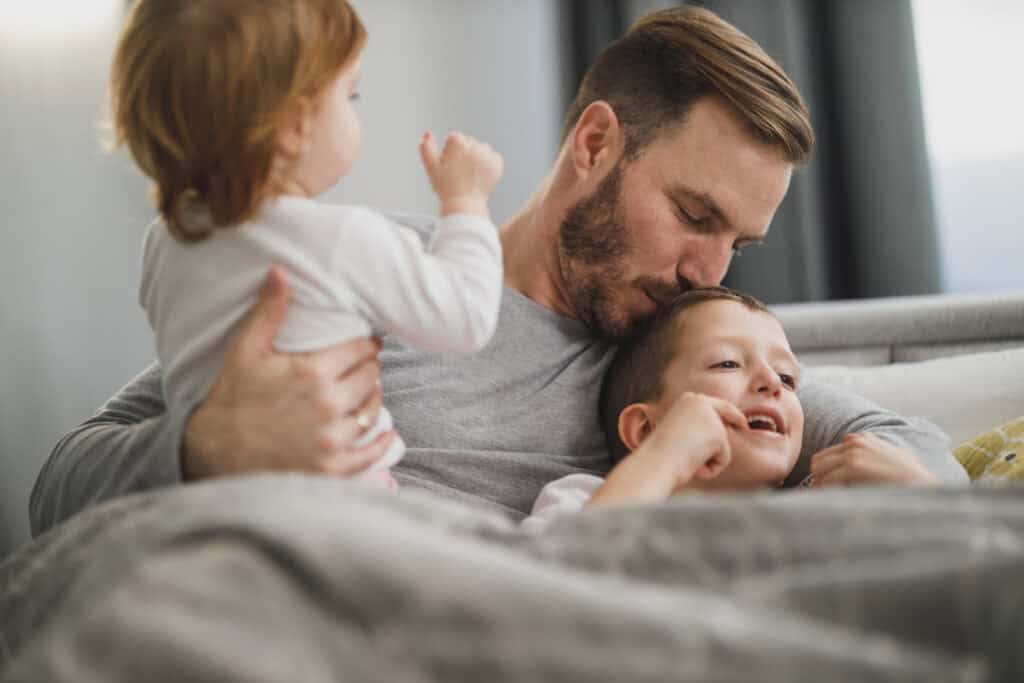 dad holding two kids, kissing son's head