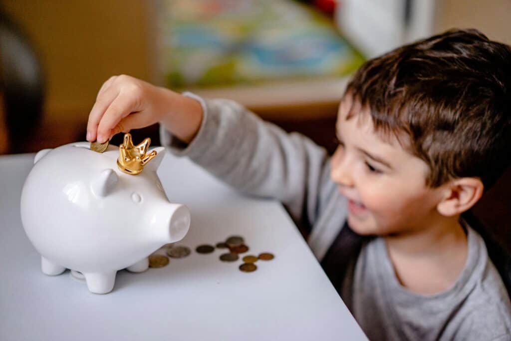 boy smiling putting money in piggy bank