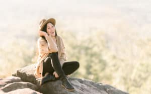 help others find hope - a teen girl sitting on a large boulder in a blurred field